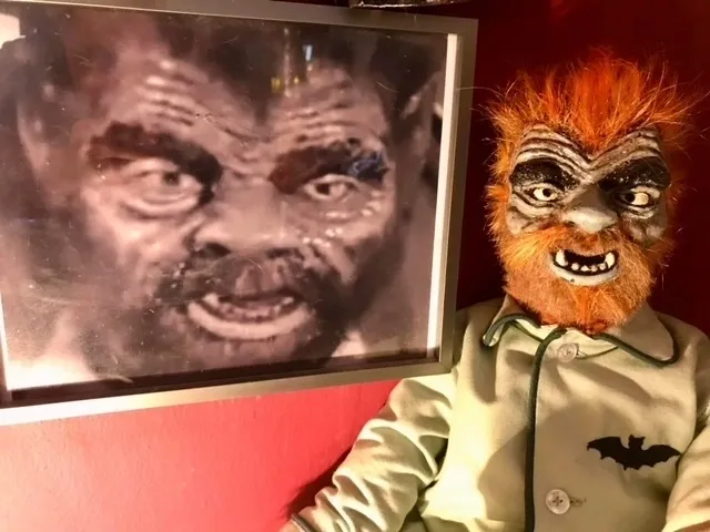 A man in a werewolf mask next to a painting.