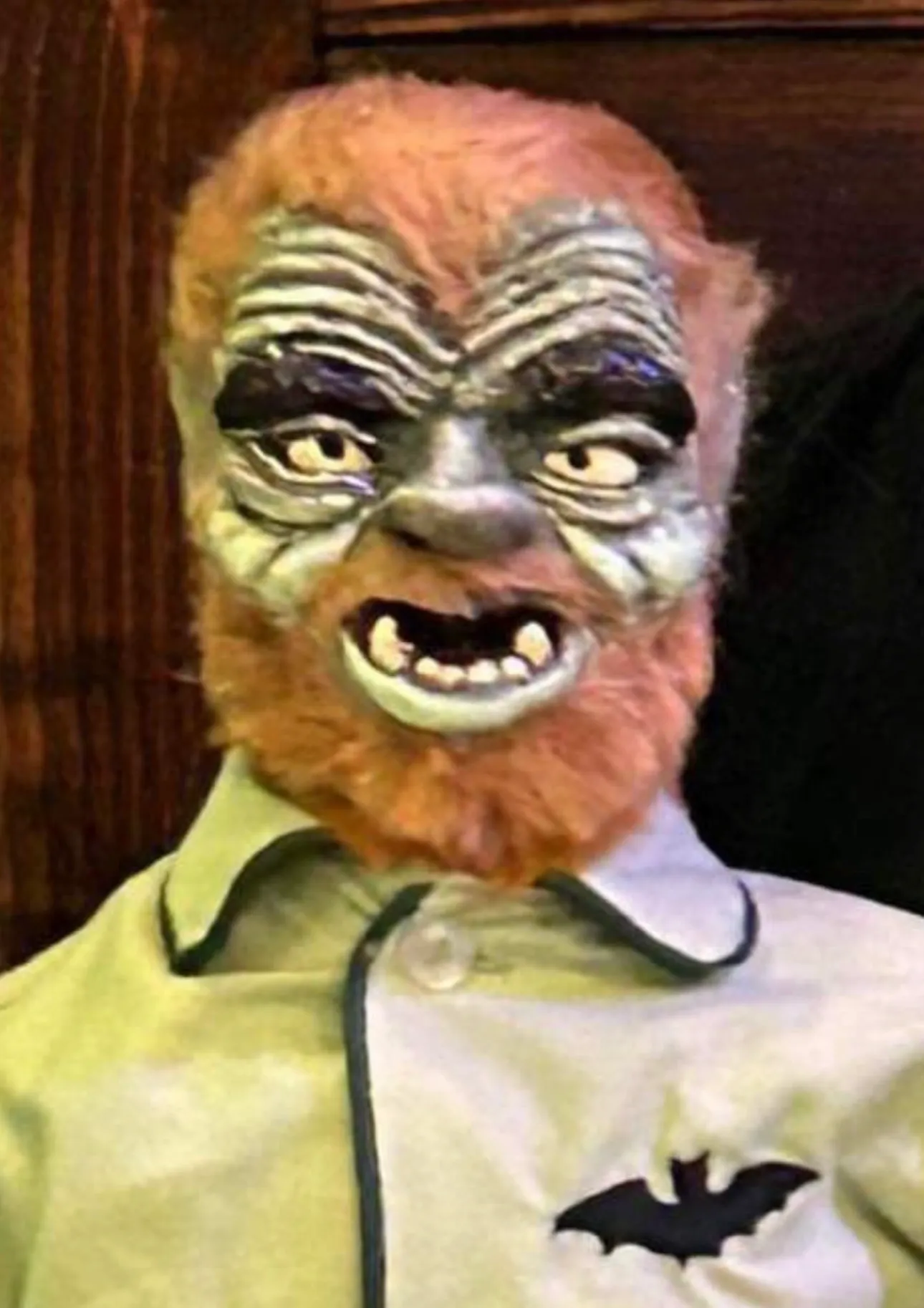 A man with a fake beard and face is wearing a werewolf mask.